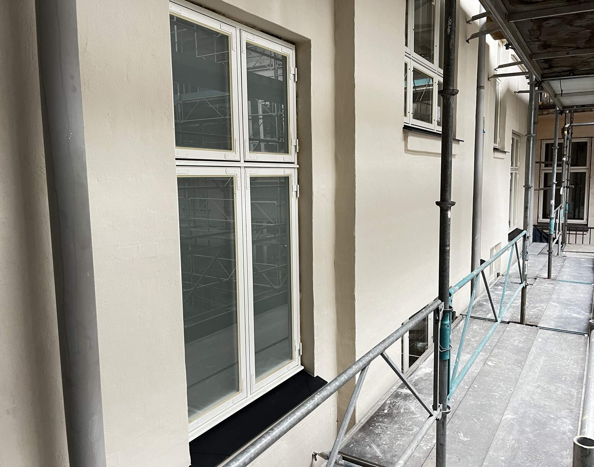 Facaderenovering af etageejendom for en andelsforening - nypudset facade med hvide vinduer set fra stilladset