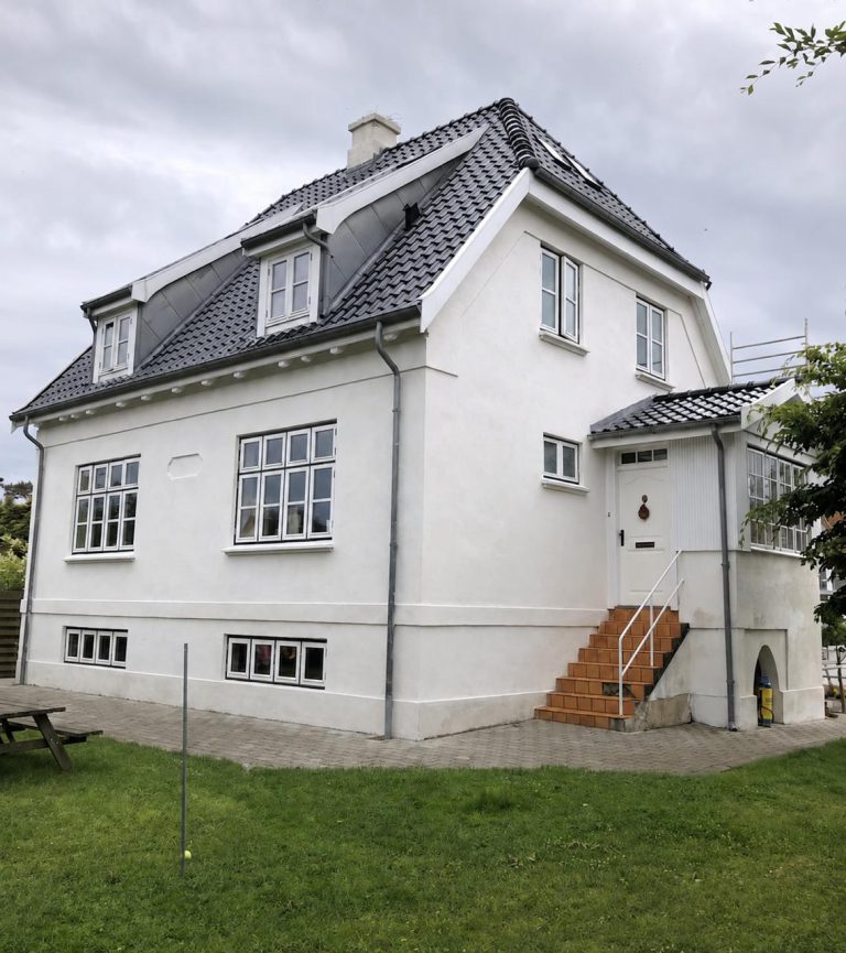 Hvidpudset villa med nyt tegltag, hvide sprossevinduer og renoveret facade i klassisk dansk stil.
