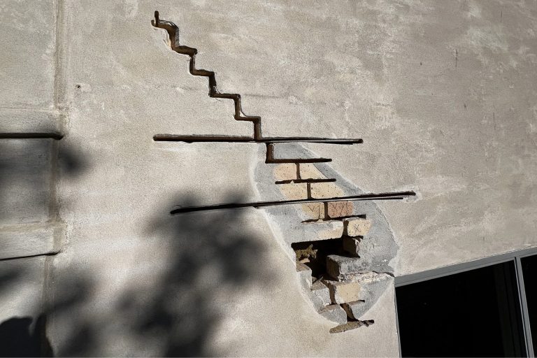 Diagonal sætningsrevne fra hjørnet af et vindue op gennem fugerne på en ældre rød murstensfacade, lineal holdt ved siden til størrelse