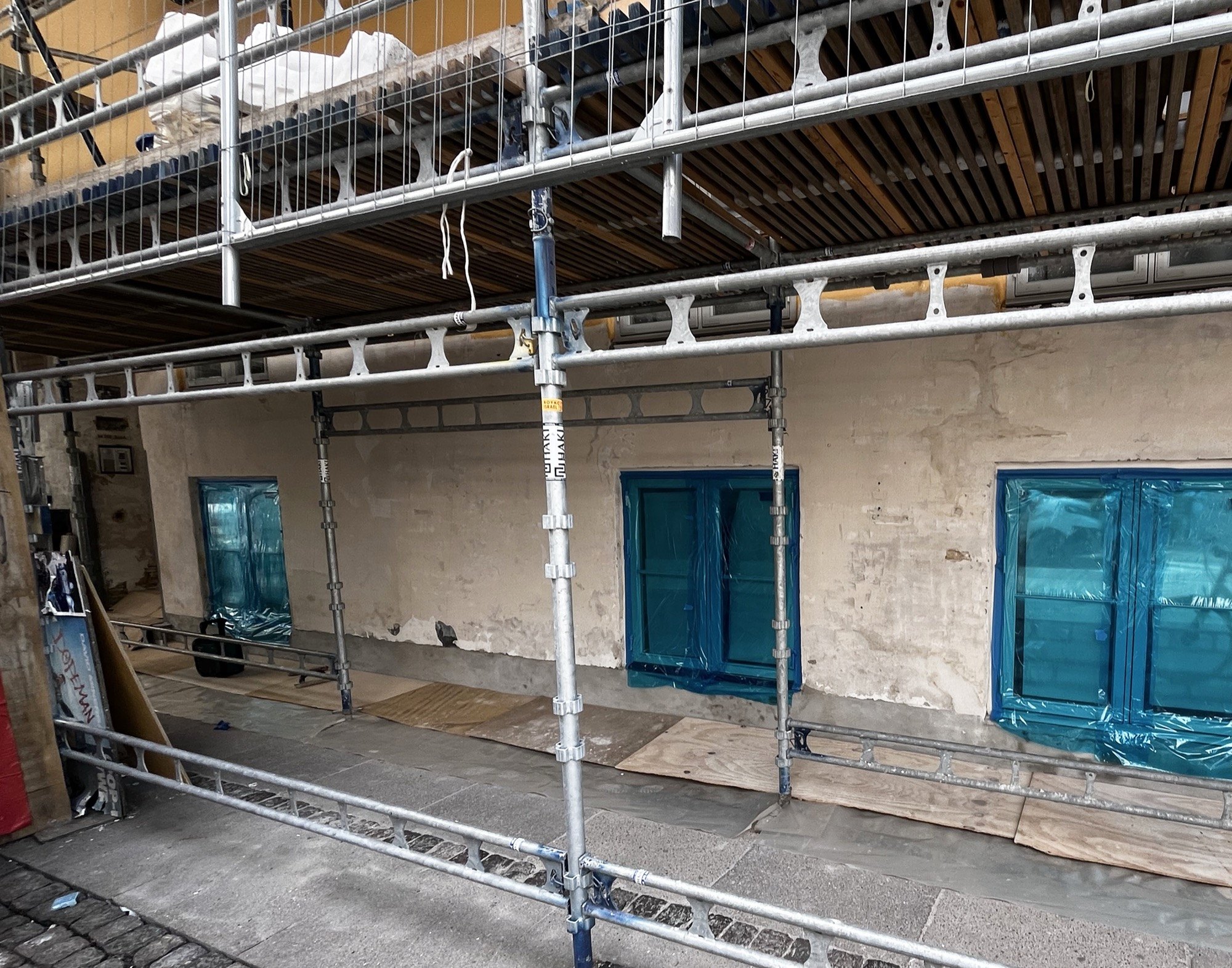Stillads opstillet på en ældre facade under renovering, vinduer afdækket